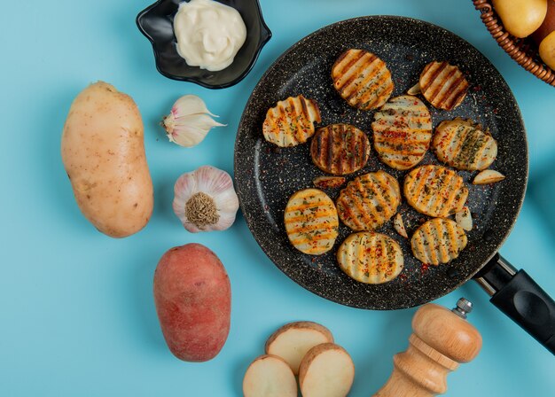 Vue de dessus des tranches de pommes de terre frites dans une poêle avec une mayonnaise non cuite sel à l'ail sur bleu