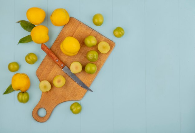 Vue de dessus des tranches de prunes cerises vertes sur une planche de cuisine en bois avec des pêches jaunes isolé sur fond bleu avec espace copie