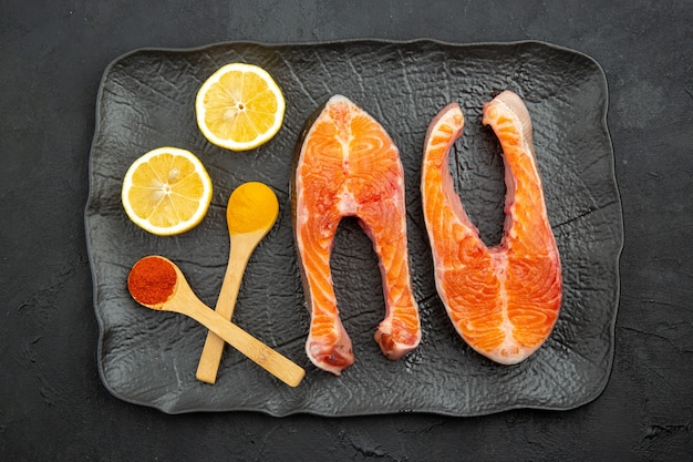 Vue de dessus des tranches de viande fraîche à l'intérieur de la plaque avec du citron sur fond sombre