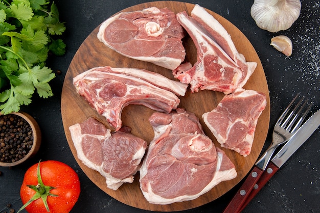 Vue de dessus des tranches de viande fraîche de viande crue avec des verts et des tomates sur un repas de cuisine sombre nourriture vache plat de nourriture salade barbecue animal