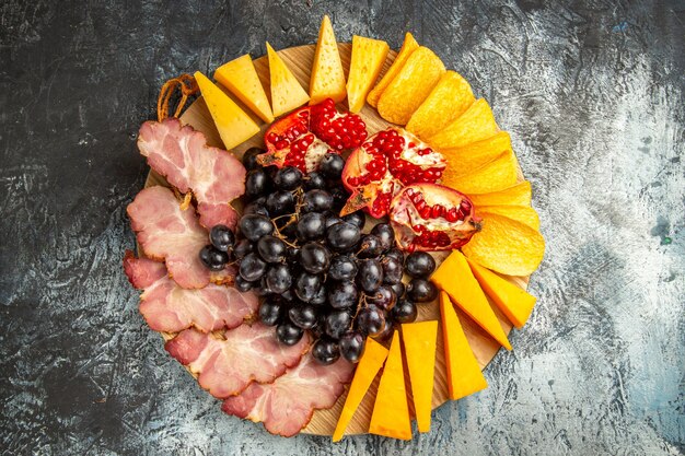 Vue de dessus des tranches de viande, des raisins au fromage et de la grenade sur un plateau de service ovale sur une surface sombre