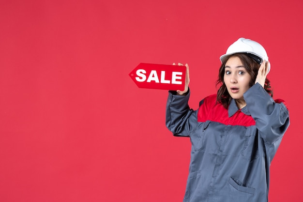 Vue de dessus d'une travailleuse choquée en uniforme portant un casque et pointant l'icône de vente sur fond rouge isolé