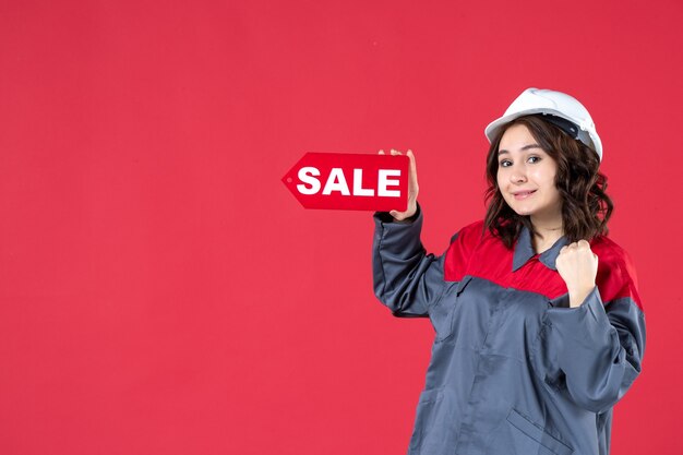 Vue de dessus d'une travailleuse confiante en uniforme portant un casque et pointant l'icône de vente sur fond rouge isolé