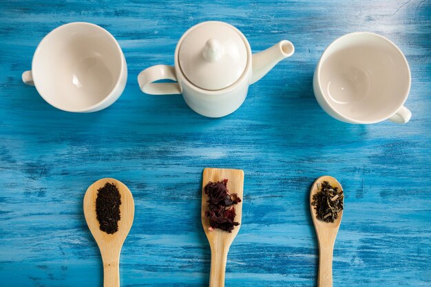 Vue de dessus de trois tasses de thé sur fond de bois bleu vintage à côté de trois cuillères de feuilles de thé