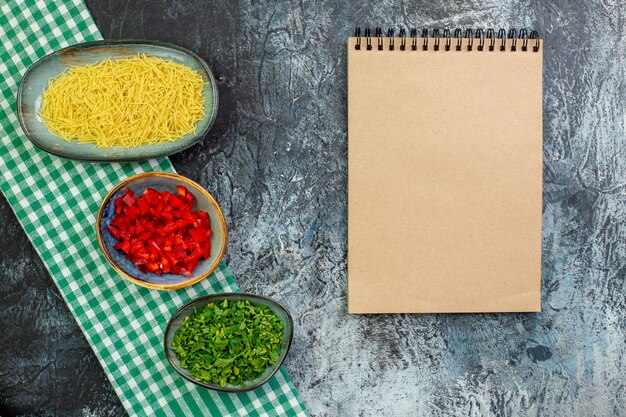 Vue de dessus des vermicelles crus avec des verts et du poivron tranché sur une table grise