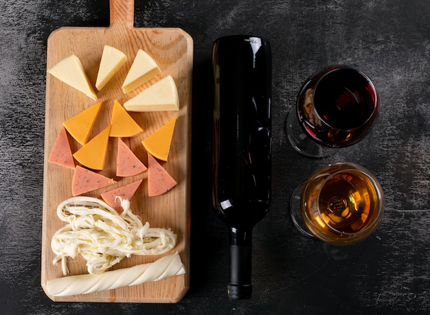 Vue de dessus des verres à vin et du fromage sur une planche à découper en bois sur horizontal sombre