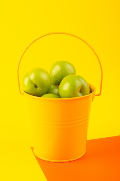 Une vue de dessus vert cerise-prune à l'intérieur du panier jaune sur le fond orange et jaune fruit aigre composition