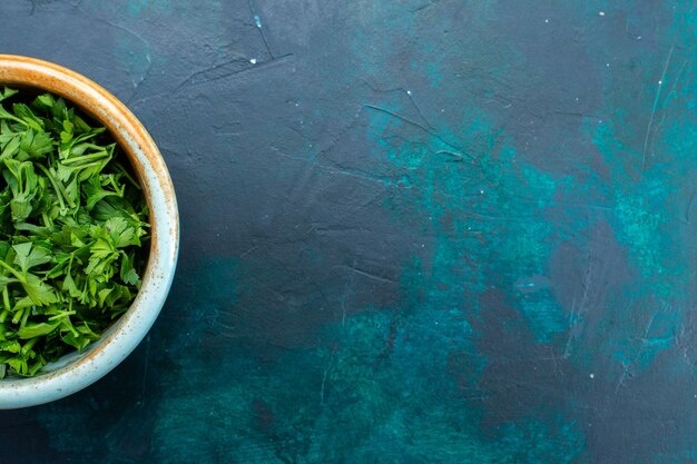 Vue de dessus des verts frais à l'intérieur du pot rond sur le bureau bleu foncé.