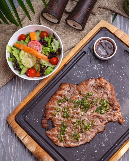 Vue de dessus de la viande de côtelette grillée avec salade de légumes et sauce sur tableau noir