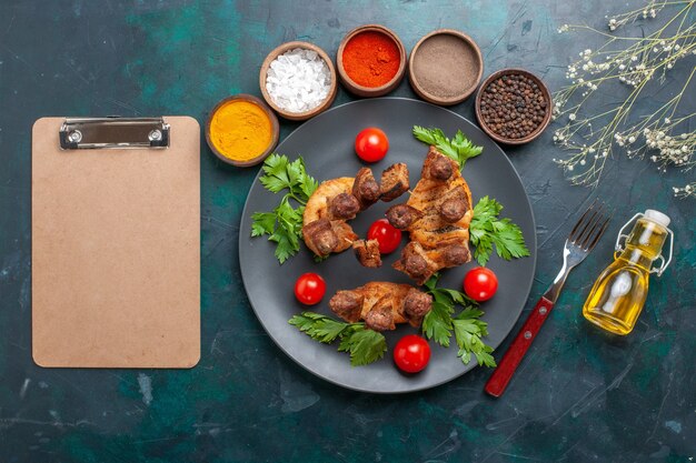 Vue de dessus de la viande cuite en tranches avec de l'huile de tomates cerises vertes et assaisonnements sur bureau bleu