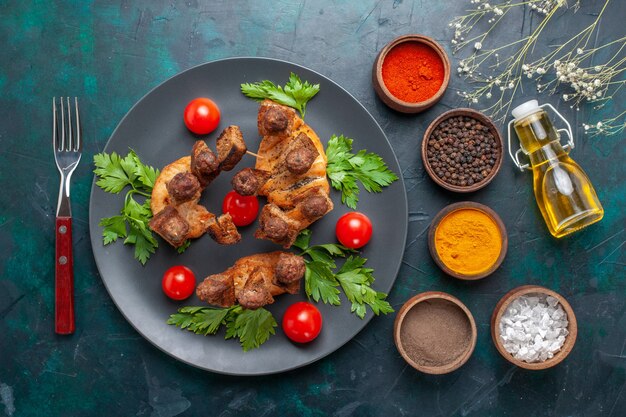 Vue de dessus de la viande cuite en tranches avec des tomates cerises à l'intérieur de la plaque et avec des assaisonnements sur le fond bleu foncé