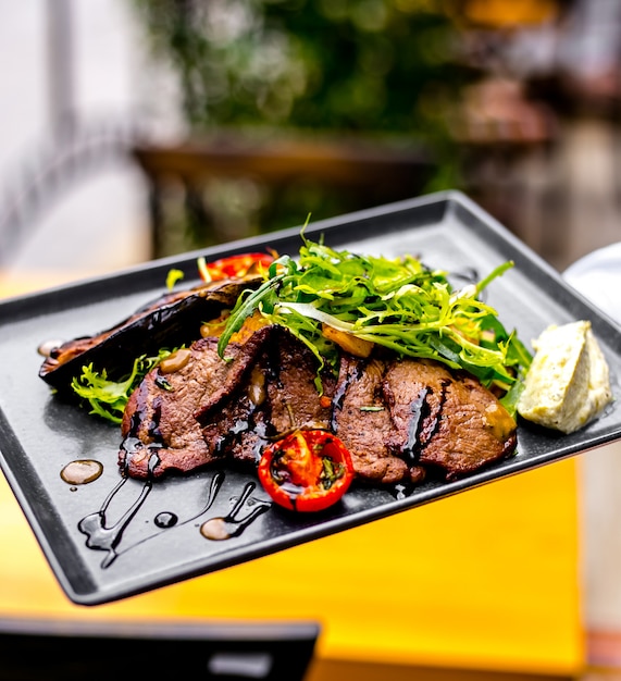 Vue de dessus de la viande frite avec tomate aubergine et roquette dans une sauce sur un plateau