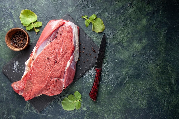 Vue de dessus de la viande rouge fraîche crue sur une planche à découper du poivre et un couteau sur fond de couleurs de mélange vert noir