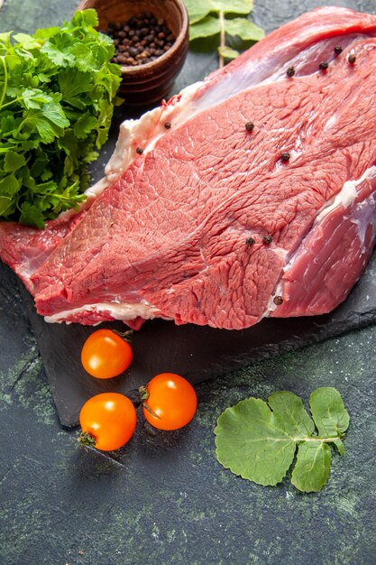 Vue de dessus de la viande rouge fraîche crue sur une planche à découper des tomates au poivre sur fond de couleurs vertes et noires