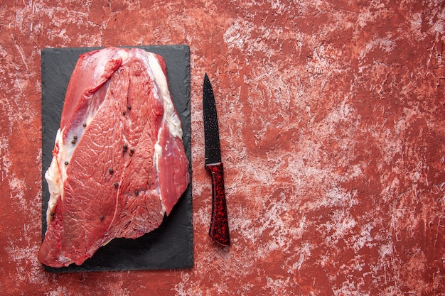 Vue De Dessus De La Viande Rouge Fraîche Crue Sur Tableau Noir Et Couteau Sur Le Côté Droit Sur Fond Rouge Pastel à L'huile Avec Espace Libre