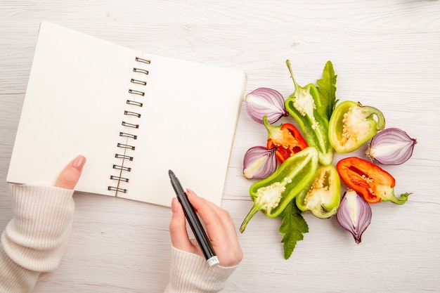 Vue de dessus de la vie saine écrit par une femme avec des légumes sur un bureau blanc