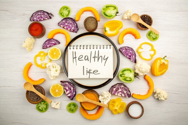 Vue de dessus une vie saine écrite sur ordinateur portable sur une assiette ronde couper les légumes différentes épices dans de petits bols sur une surface blanche