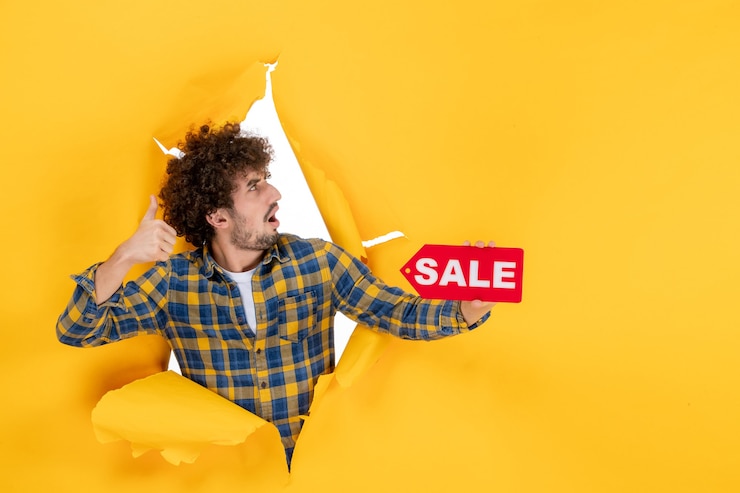Photo gratuit vue de devant jeune homme tenant une vente rouge écrivant sur un fond déchiré jaune