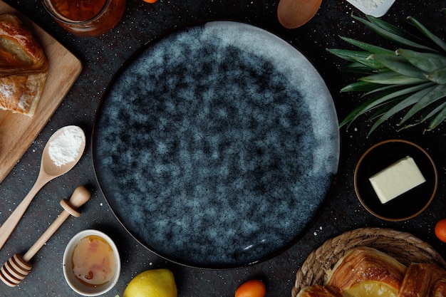 Vue du dessus de l'assiette vide avec confiture citron kumquats croissants farine beurre feuilles d'ananas sur fond noir