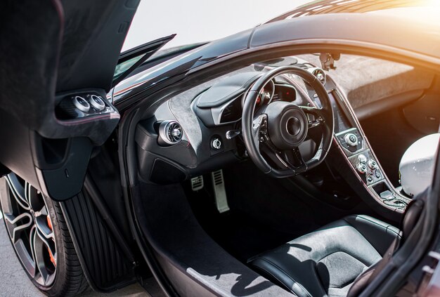 Vue du salon côté avant d'une voiture de sport noire, roue noire avec direction argent métallisé, direction, porte ouverte.