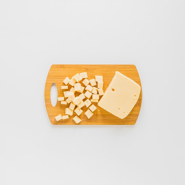 Une vue en élévation de cubes de fromage sur une planche à découper en bois sur fond blanc