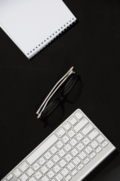 Une vue en élévation du bloc-notes en spirale; lunettes et clavier sur le bureau noir