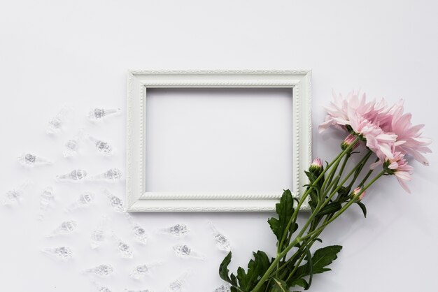 Vue en élévation du cadre d&#39;image vide; coquilles de cristal et fleurs roses sur une surface blanche