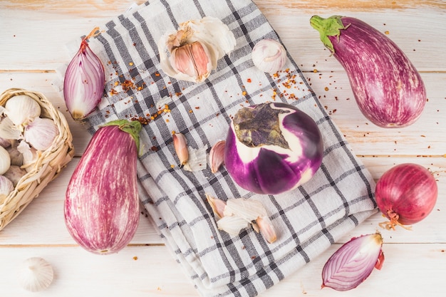 Vue élevée des aubergines; oignon; gousses d&#39;ail et chiffon à carreaux sur planche de bois