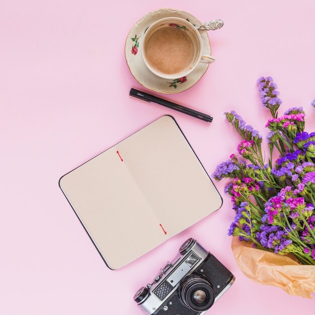 Une vue élevée du bouquet de fleurs; appareil photo vintage; journal intime; stylo et tasse à café sur fond rose