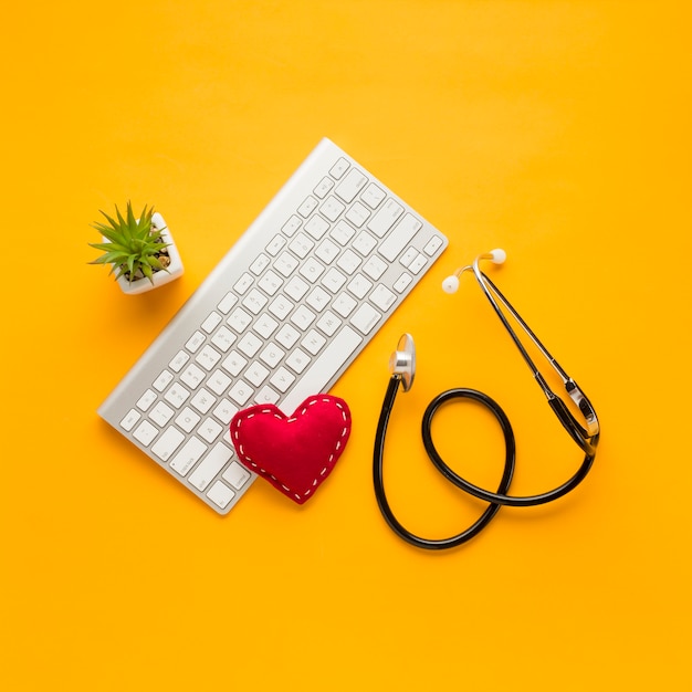 Vue élevée du stéthoscope; en forme de cœur cousu; clavier sans fil; plante succulente sur fond jaune