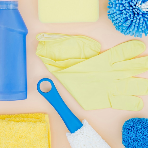 Une vue élevée de gants jaunes; éponge; bouteille; serviette de table sur fond de pêche