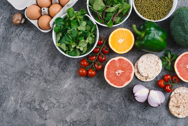 Une vue élevée de légumes; des œufs; agrumes et gâteau de riz soufflé sur fond de béton gris