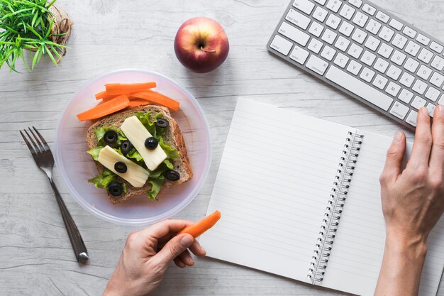 Vue élevée de la main de la personne tenant des aliments sains tout en travaillant sur le clavier