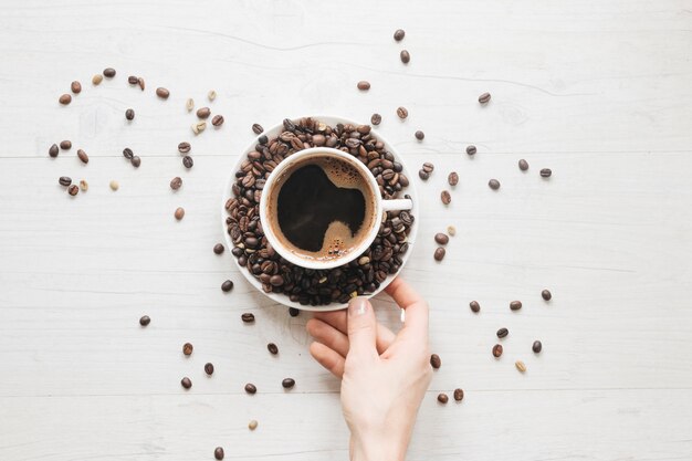 Une vue élevée de la main d&#39;une personne tenant une soucoupe avec des grains de café et une tasse de café