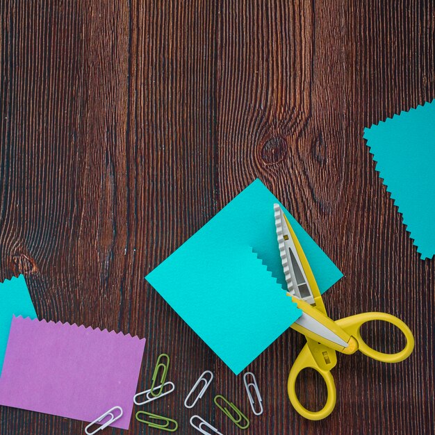 Vue élevée de papiers colorés; trombones et ciseaux sur un bureau en bois