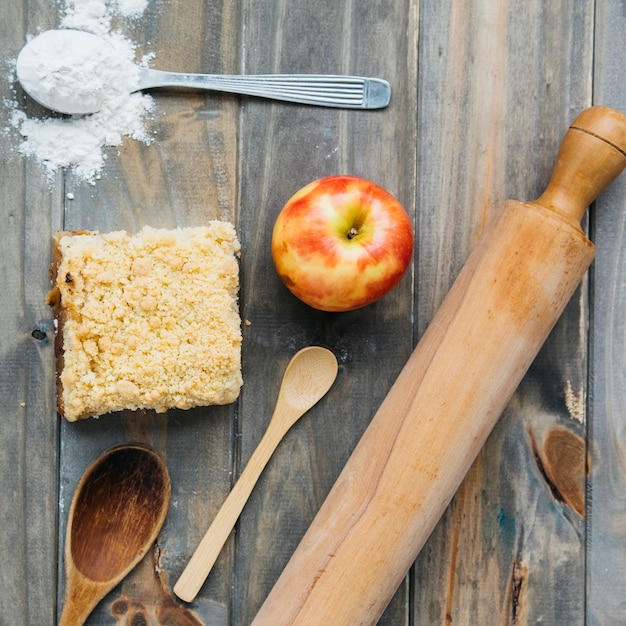 Photo gratuite vue élevée de la pâtisserie; pomme; farine; rouleau à pâtisserie et une cuillère sur une surface en bois