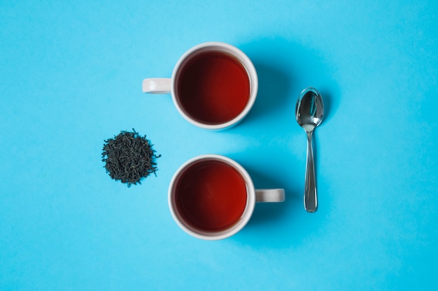 Une vue élevée de tasses à thé à base de plantes noir et cuillère sur fond bleu