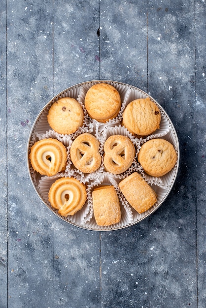 Vue éloignée du haut de délicieux biscuits sucrés différents formés à l'intérieur de l'emballage rond sur un bureau gris, biscuit biscuit gâteau sucré au sucre