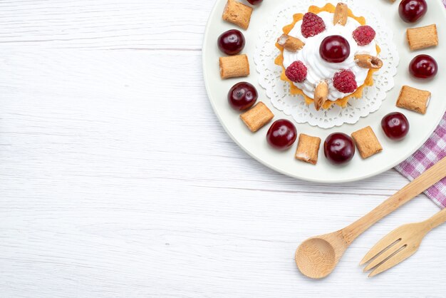 Vue éloignée du haut du petit gâteau crémeux aux framboises et petits biscuits sur un bureau blanc, gâteau aux fruits crème de baies sucrées