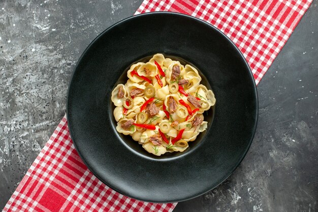 Vue d'ensemble de délicieuses conchiglie au poivre sur une assiette noire et un couteau sur une serviette dénudée rouge sur fond gris