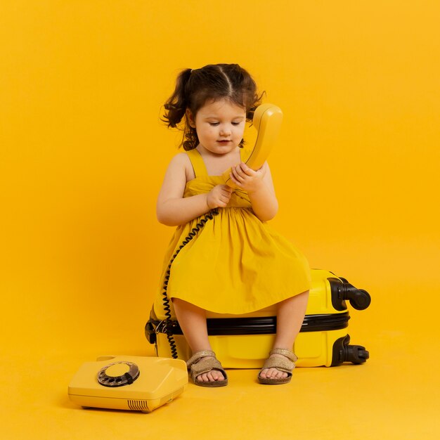 Vue de face de l'adorable enfant posant avec téléphone et bagages