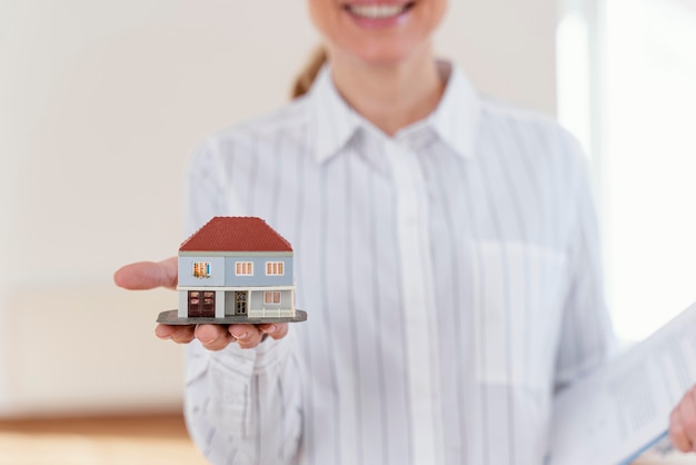 Vue de face de l'agent immobilier féminin défocalisé smiley montrant maison miniature