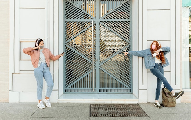 Vue de face des amies avec des masques faciaux à l'extérieur à l'aide de smartphones et de danse