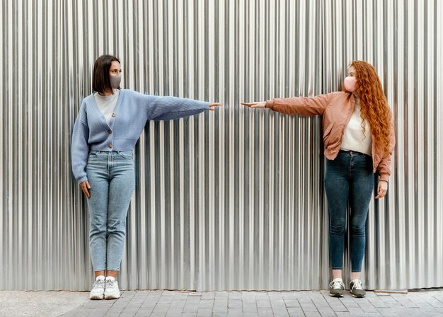 Vue de face des amies avec des masques faciaux à l'extérieur toucher les doigts