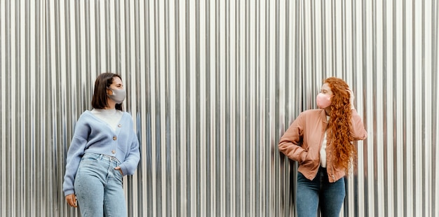 Vue de face des amies avec des masques faciaux à l'extérieur