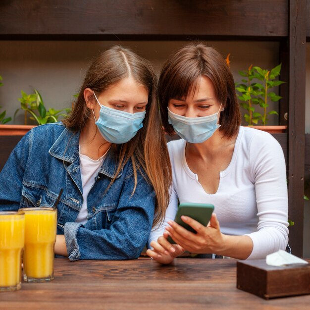 Vue de face des amies regardant smartphone tout en ayant du jus