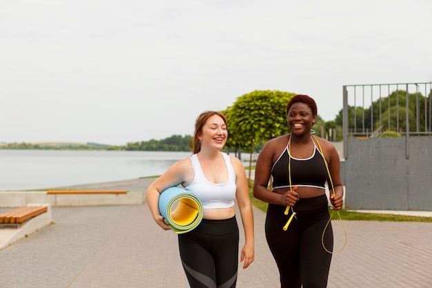 Vue de face d'amies smiley à l'extérieur essayant de faire de l'exercice