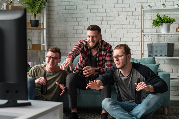 Vue de face des amis masculins à regarder les sports à la télévision ensemble