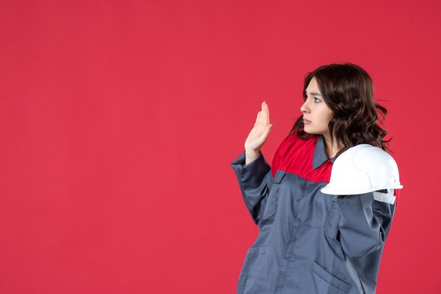 Vue de face de l'architecte femme confus tenant un casque et debout sur un mur rouge isolé