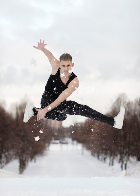 Vue de face de l'artiste masculin hip hop posant dans les airs avec de la neige